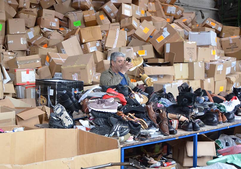 Ein Mann handsortiert Schuhe mit einem Berg von Pappkartons im Hintergrund
